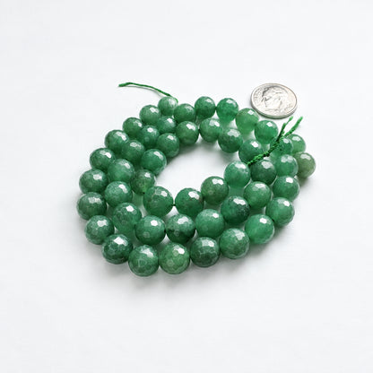 Faceted green gemstone beads on a white background with a US quarter coin for scale.