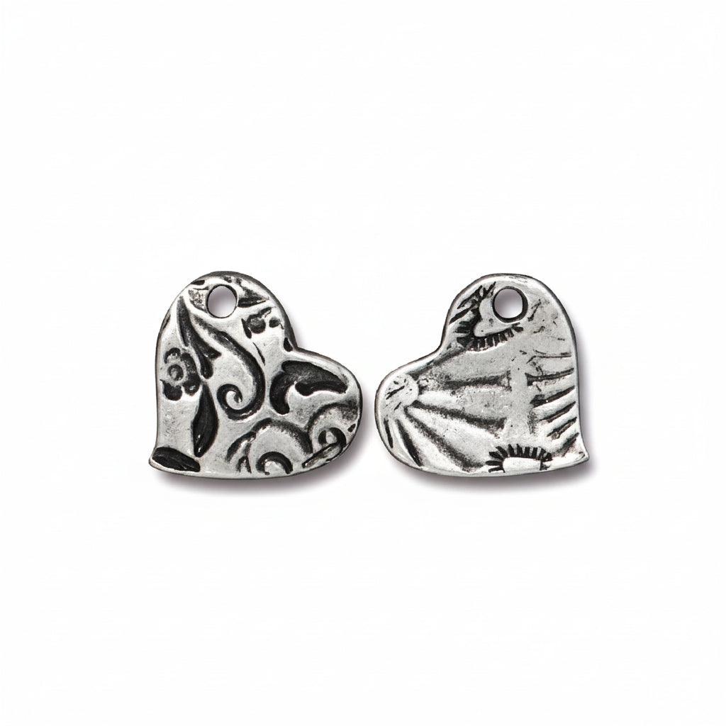 Two silver heart-shaped metal charms with engraved floral and sunburst patterns, shown on a plain white background.