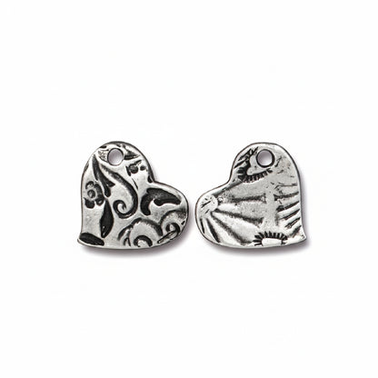 Two silver heart-shaped metal charms with engraved floral and sunburst patterns, shown on a plain white background.