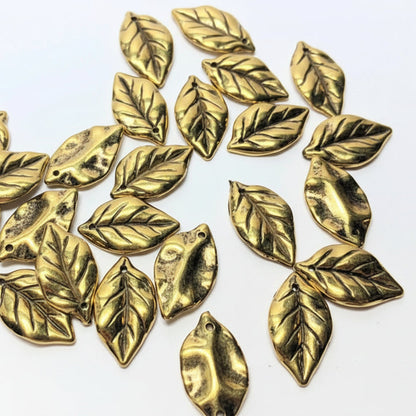 A collection of metallic gold leaf-shaped craft beads scattered on a plain white background.