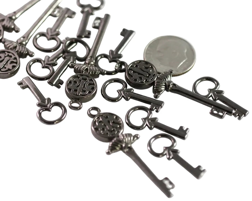 A group of antique-style metal key charms with circular monogram pendants, displayed on a white background next to a US quarter for scale.
