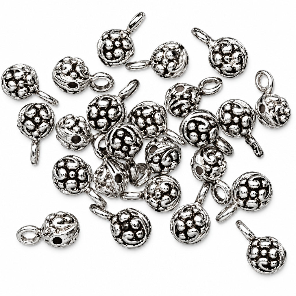 A pile of silver-toned metal charm beads with a textured, floral embossed pattern and a small loop at the top, shown on a plain white background.