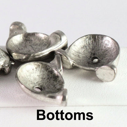 Close-up of several small metallic silver bowl-shaped components with a textured finish and a hole, labeled 'Bottoms' on a white background.