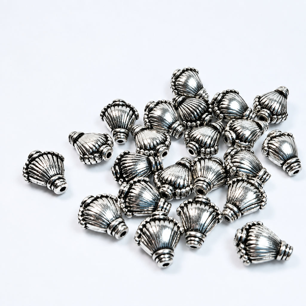 A pile of small metallic silver decorative beads with a textured, shell design, arranged on a plain white background.