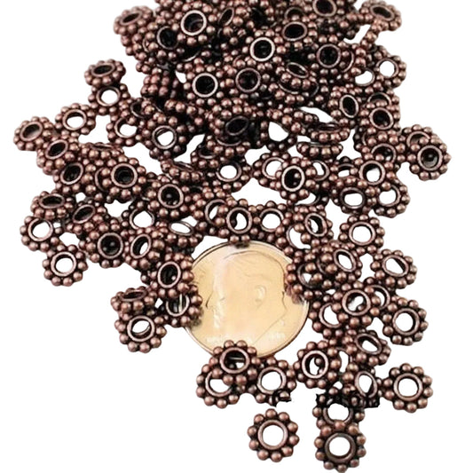 A pile of small metallic bronze spacer beads with circular cutouts, shown on a white background with a coin for scale.