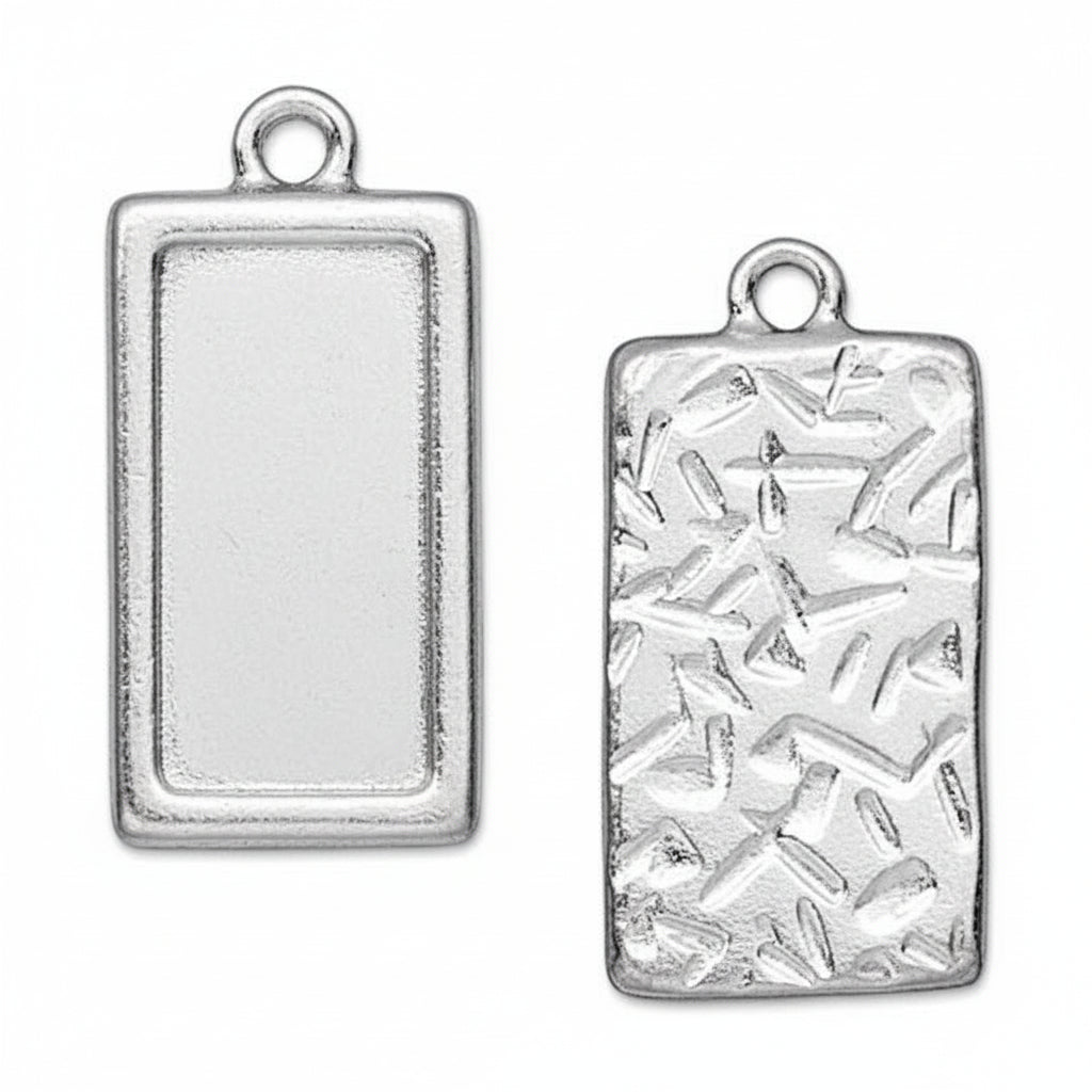Two silver rectangular charms with rounded corners and top loops, shown side by side on a white background. The left charm has a smooth textured center with engraved diagonal lines, and the right charm has a raised abstract geometric pattern.