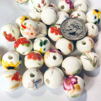White ceramic beads with colorful hand-painted floral and botanical designs, shown with a US dime for scale on a white background.