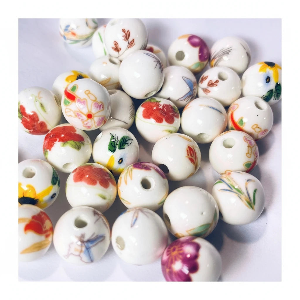 A pile of round white ceramic beads with hand-painted floral and butterfly designs in red, yellow, green, and purple, shown on a white background.