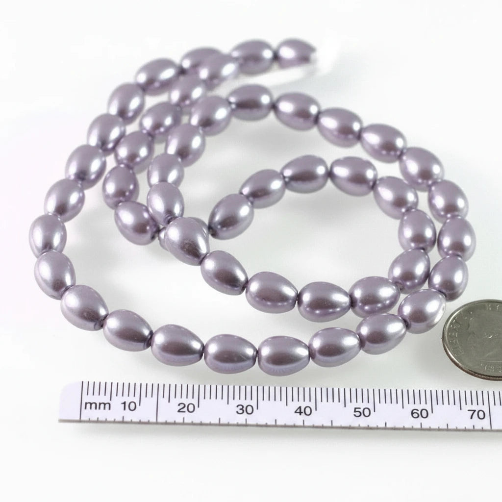A strand of glossy, teardrop-shaped beads in a dusty lavender-purple color, displayed on a white background with a ruler and a coin for scale.