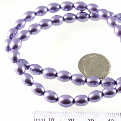 A strand of glossy, oval-shaped purple beads coiled on a white surface, with a US quarter coin and a centimeter ruler included for scale.