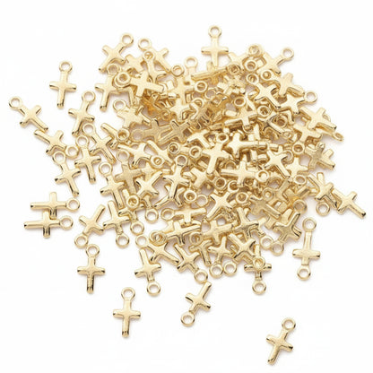Gold cross-shaped jewelry findings with loop tops, scattered on a dark gray background with a circular inset showing a larger single piece.