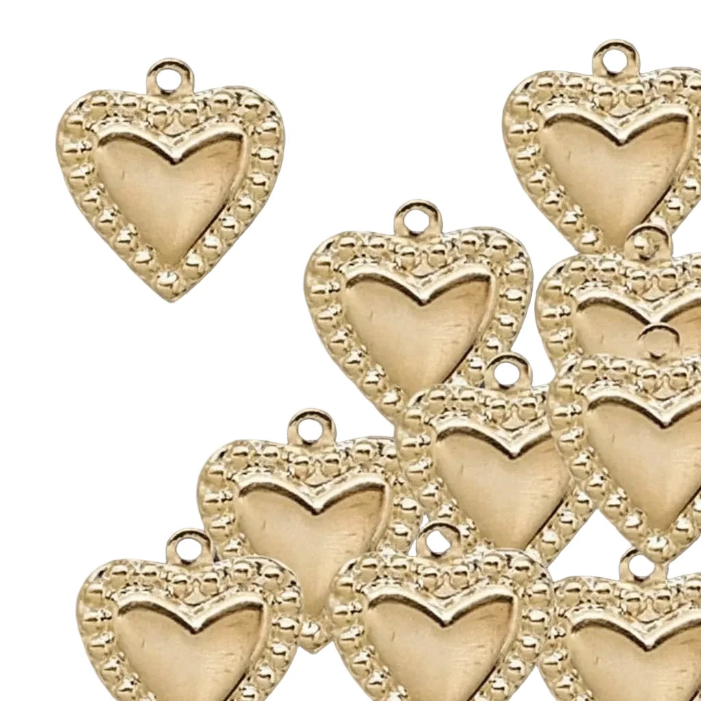 A set of gold heart-shaped jewelry charms with a beaded border and a smaller hollow heart cutout in the center, shown on a solid dark gray background.