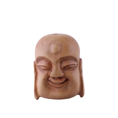 A carved wooden Buddha head sculpture with a smooth, bald forehead, closed eyes, and a gentle smile, set against a solid light purple background.
