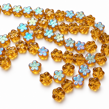 A strand of translucent amber glass beads shaped like four-leaf clovers, with some beads featuring iridescent pastel blue and white centers, displayed on a plain white surface.
