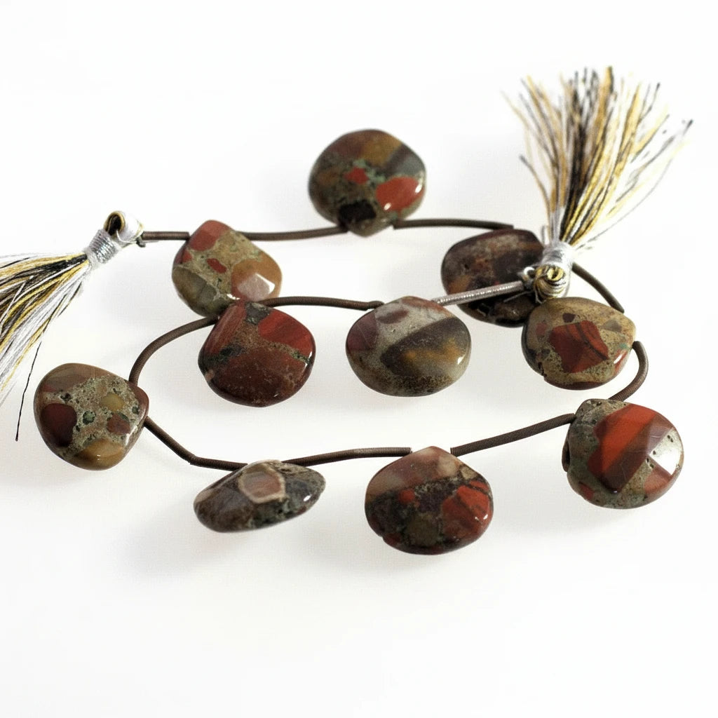 A strand of polished natural stone beads with a dark cord, featuring red, brown, and gray marbled patterns, finished with a white and gold tassel on a white background.