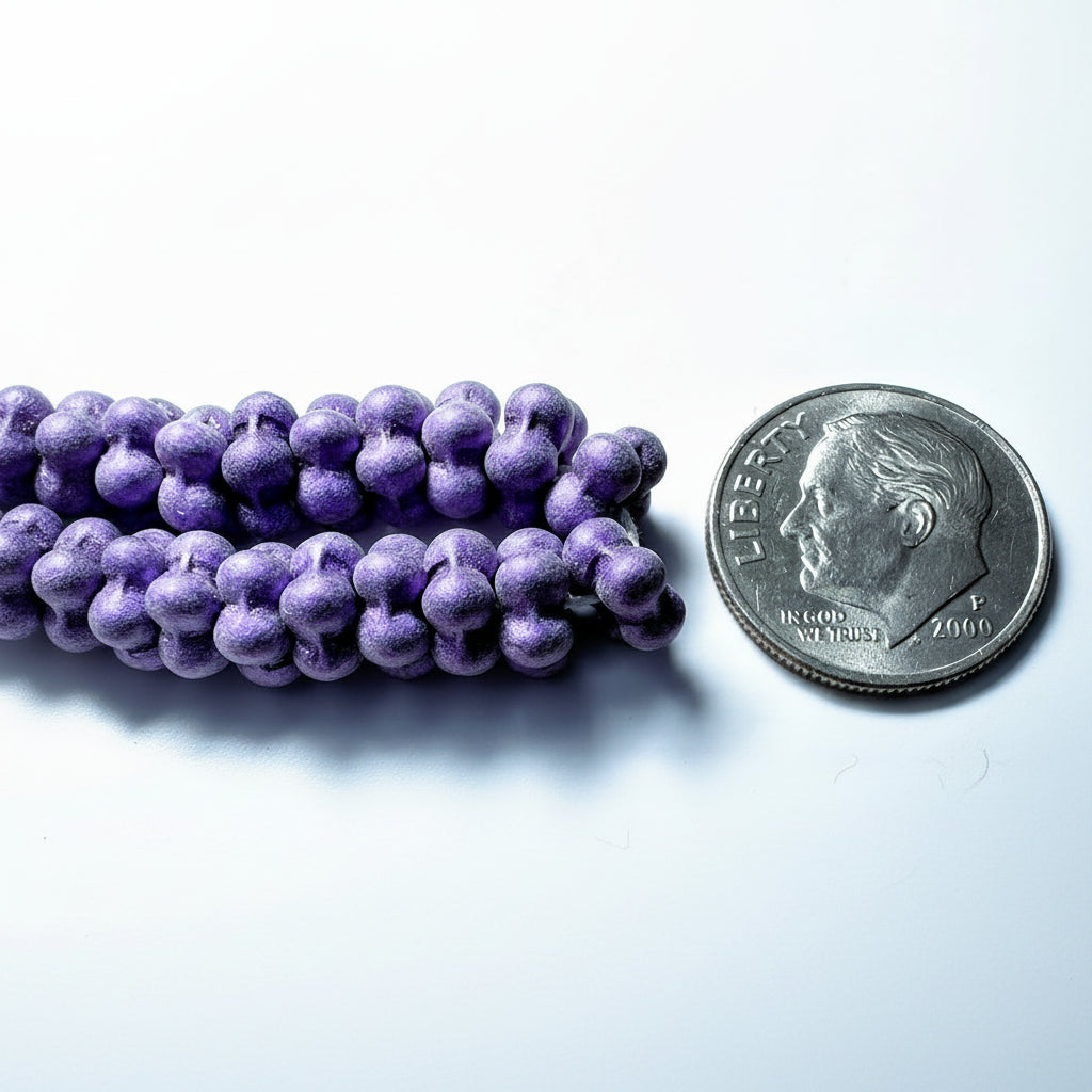 Purple grape-shaped beads arranged next to a U.S. dime for scale, on a light gray background.