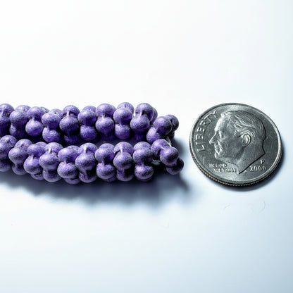 Purple grape-shaped beads arranged next to a U.S. dime for scale, on a light gray background.