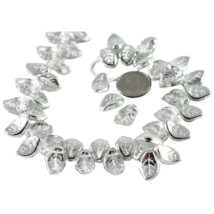 A strand of silver-toned leaf-shaped beads with clear faceted centers, arranged in a circle on a white background with a coin for scale.