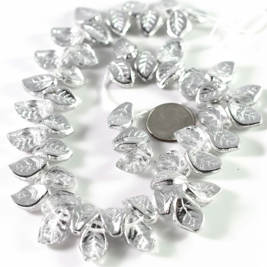 Silver leaf-shaped beads arranged in a circle on a white background, with a round coin placed in the center for scale.