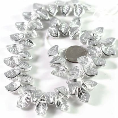 Silver leaf-shaped beads arranged in a circle on a white background, with a round coin placed in the center for scale.