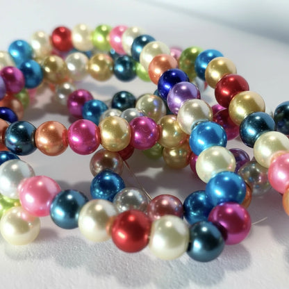 A close-up of strands of shiny, iridescent round beads in multiple colors including blue, pink, purple, gold, red, green, and white, arranged on a light surface.