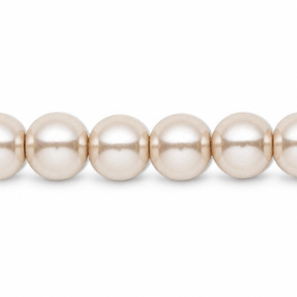 A close-up of a strand of round, lustrous pearl-like beads in a warm champagne or cream tone against a plain white background.