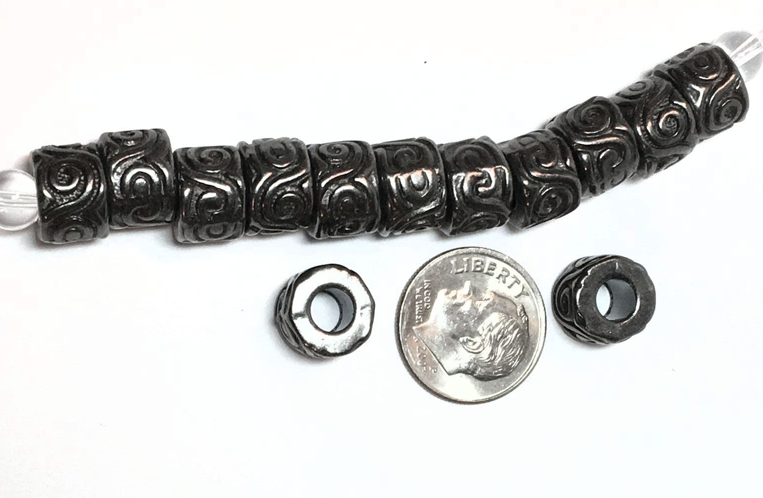 Decorative black bead with a silver bead, next to a dime for scale on a white background