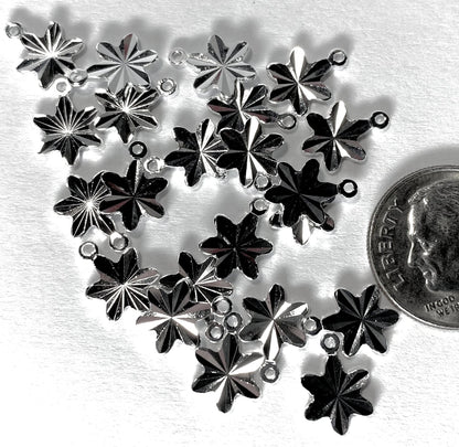 A cluster of silver-toned metal snowflake charms with small loops at the top, arranged on a white textured surface next to a US quarter for scale.