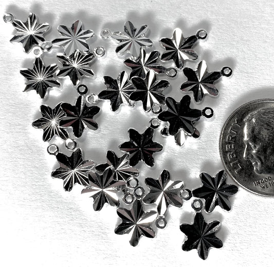 A cluster of silver-toned metal snowflake charms with small loops at the top, arranged on a white textured surface next to a US quarter for scale.