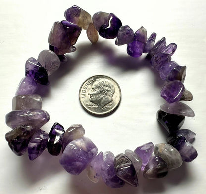 A chunky stretch bracelet made of polished tumbled purple amethyst chips, shown next to a US dime for scale on a white background.