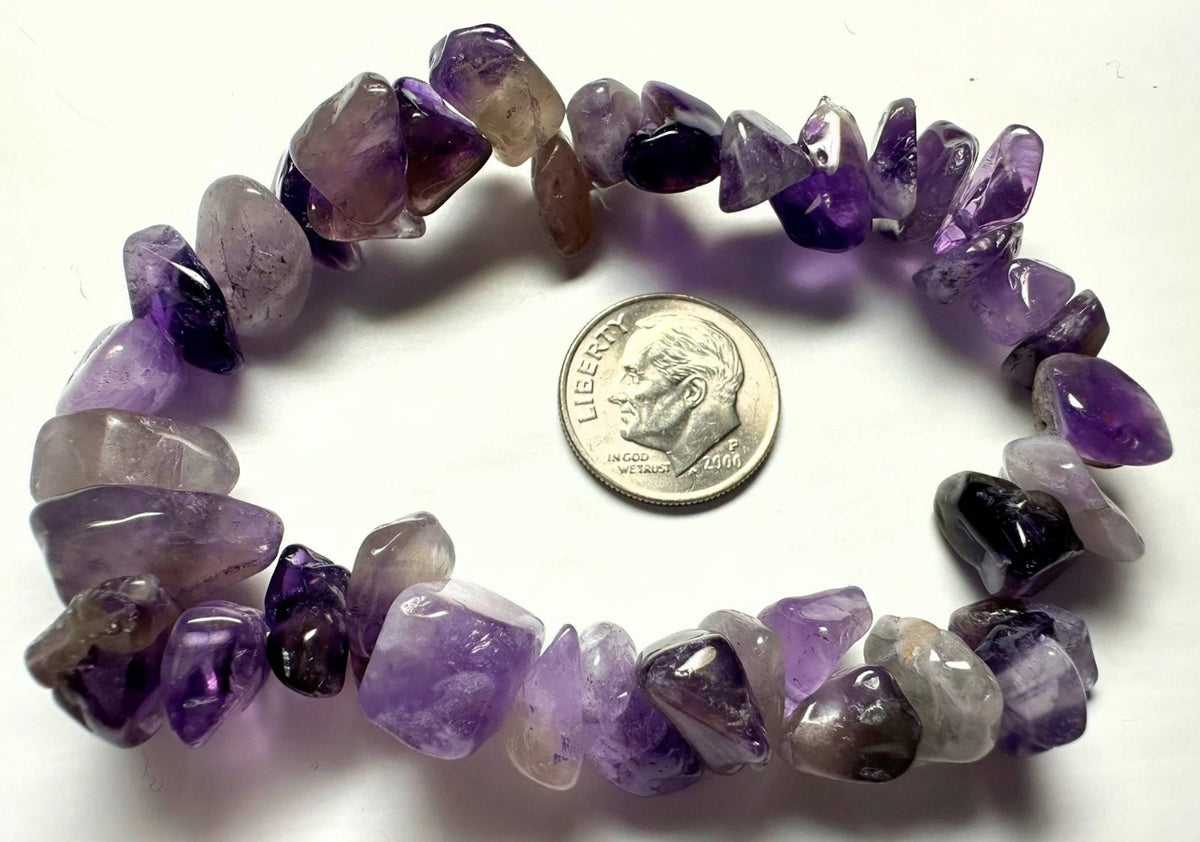 A tumbled amethyst chip bracelet arranged in a circle on a white background, with a US dime placed in the center for scale. The beads show a gradient of purple and lavender tones.