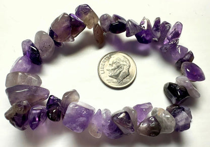A tumbled amethyst chip bracelet arranged in a circle on a white background, with a US dime placed in the center for scale. The beads show a gradient of purple and lavender tones.