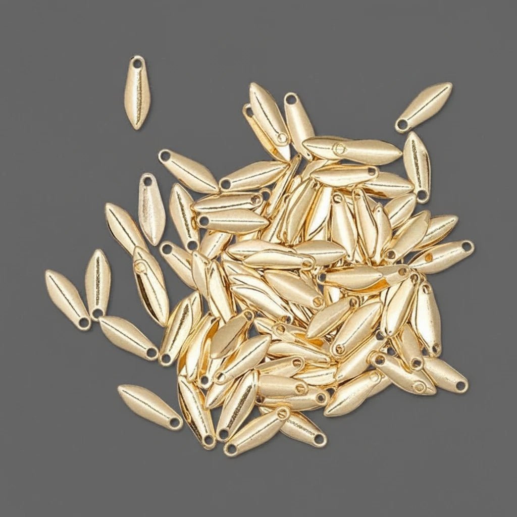 A pile of small metallic gold teardrop-shaped beads with pre-drilled holes, scattered on a dark gray background.