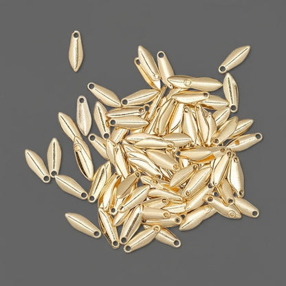A pile of small metallic gold teardrop-shaped beads with pre-drilled holes, scattered on a dark gray background.