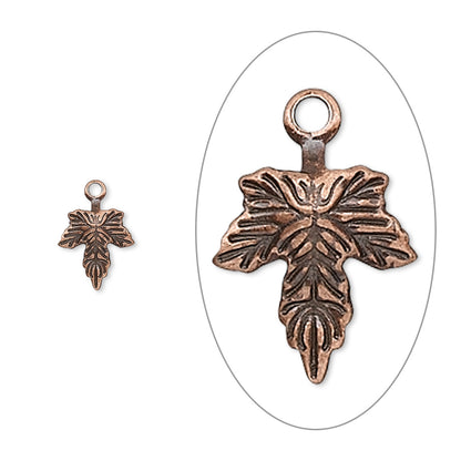 An antique bronze cross charm with an embossed floral design and a top loop, shown in a close-up inside a white oval on the right and a smaller full view on the left, against a plain white background.
