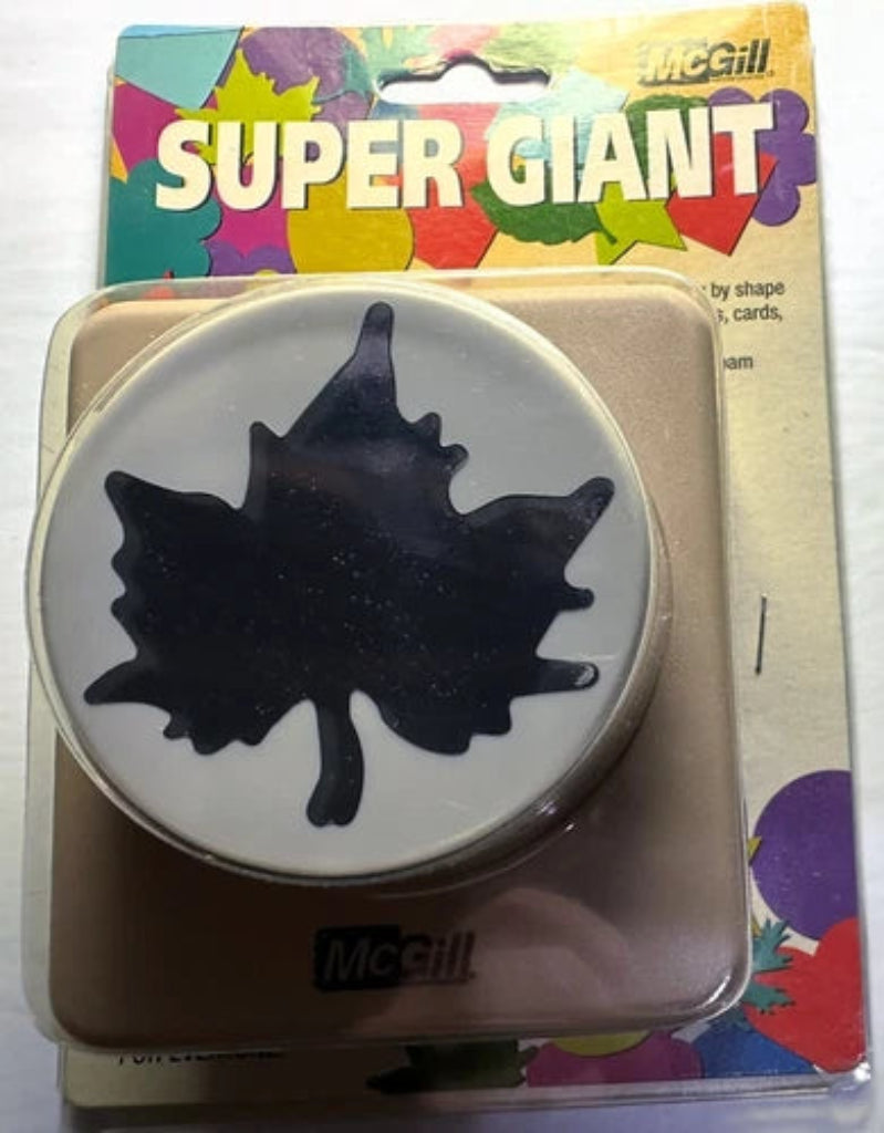 McGill Super Giant circular hole puncher with a black maple leaf design on a white circular face, packaged in its original colorful cardboard blister pack.