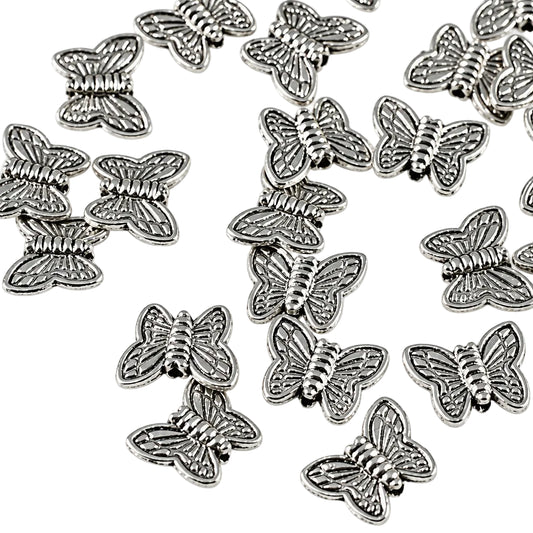 A pile of small silver butterfly-shaped charms or beads scattered on a plain white background.