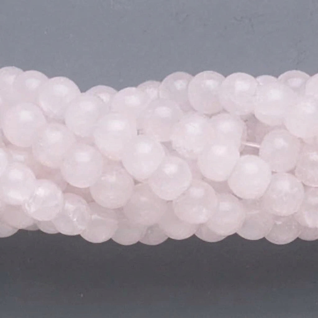 A close-up of pale pink translucent round beads strung together on a cord, set against a dark gray background.