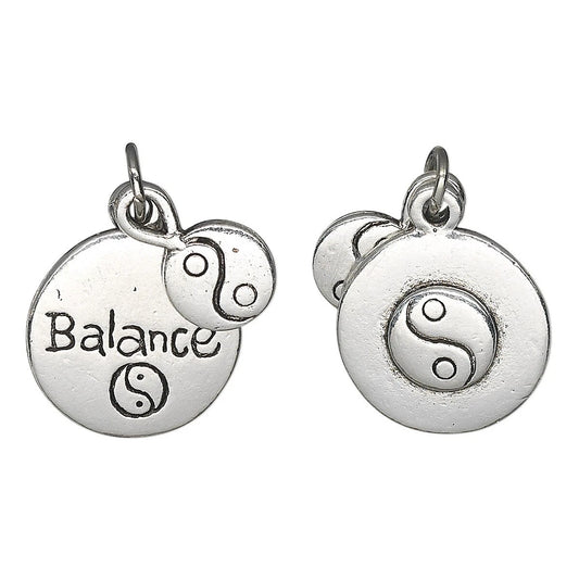 Two silver-toned round charm pendants on a white background, each with a small dangling yin-yang charm and a top loop. One pendant is engraved with the word 'Balance' and a yin-yang symbol, and the other shows a raised yin-yang symbol.