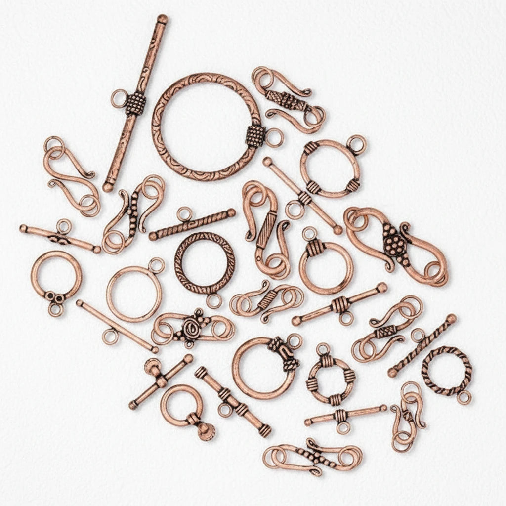 A collection of antique bronze and rose gold jewelry findings, including toggle clamps, spring rings, and loop clasps, arranged on a plain white background.