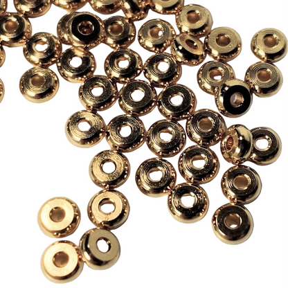 A pile of small metallic gold ring-shaped beads with a central hole, scattered on a plain white surface.