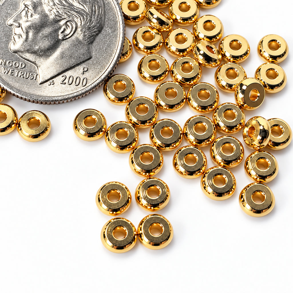 Gold metallic round spacer beads scattered on a white surface next to a US dime for scale.