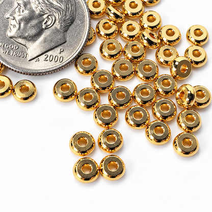 Gold metallic round spacer beads scattered on a white surface next to a US dime for scale.