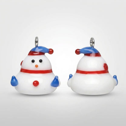 Two small snowman-shaped jewelry charms or pendants on a plain gray background. One is shown from the front and the other from the back, both white with blue and red accents.