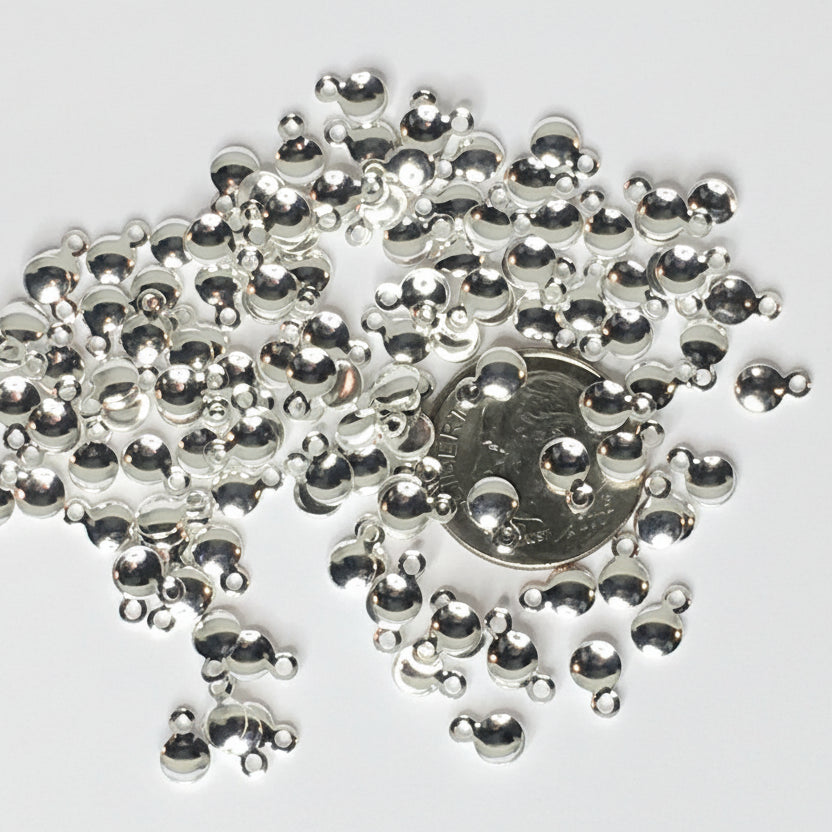 Silver metallic dome charms with small loops, scattered on a white background with a US quarter coin in the center for scale.
