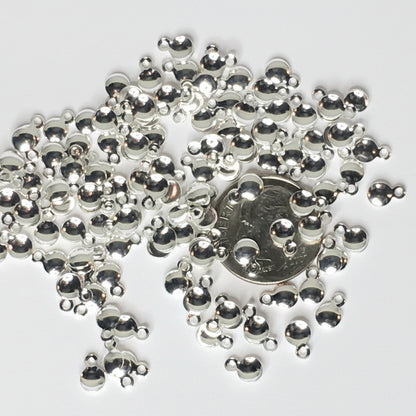 Silver metallic dome charms with small loops, scattered on a white background with a US quarter coin in the center for scale.