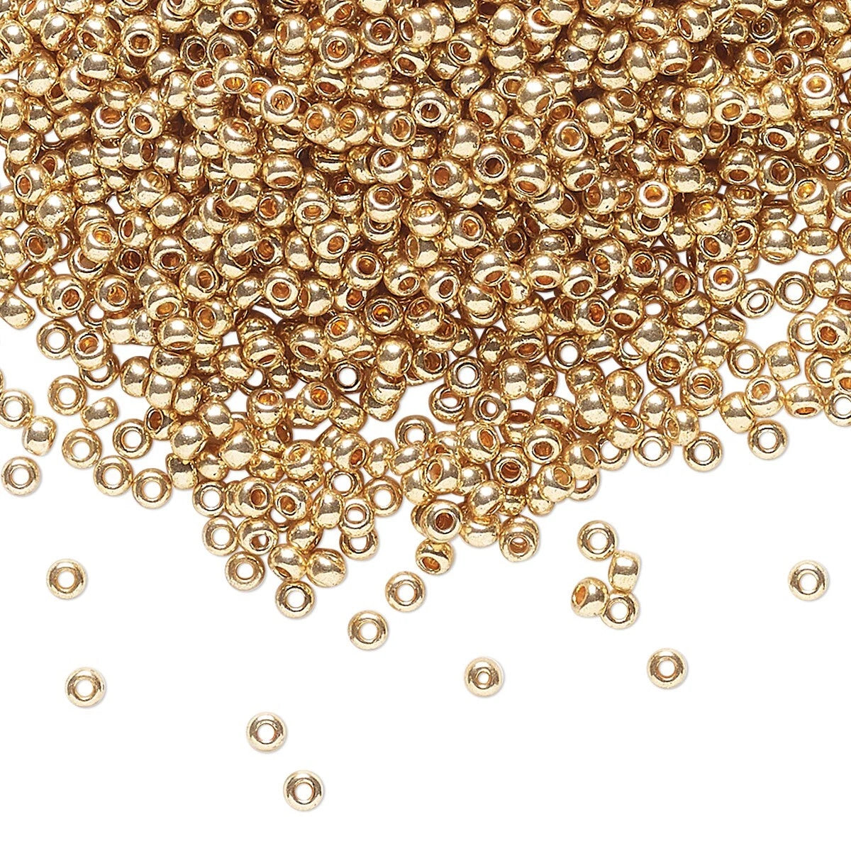 Gold metallic seed beads scattered on a white background, with more concentrated toward the top and a few beads spilled toward the bottom.