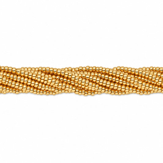 A close-up of a strand of small metallic gold faceted beads arranged in a wavy, braided pattern against a plain white background.