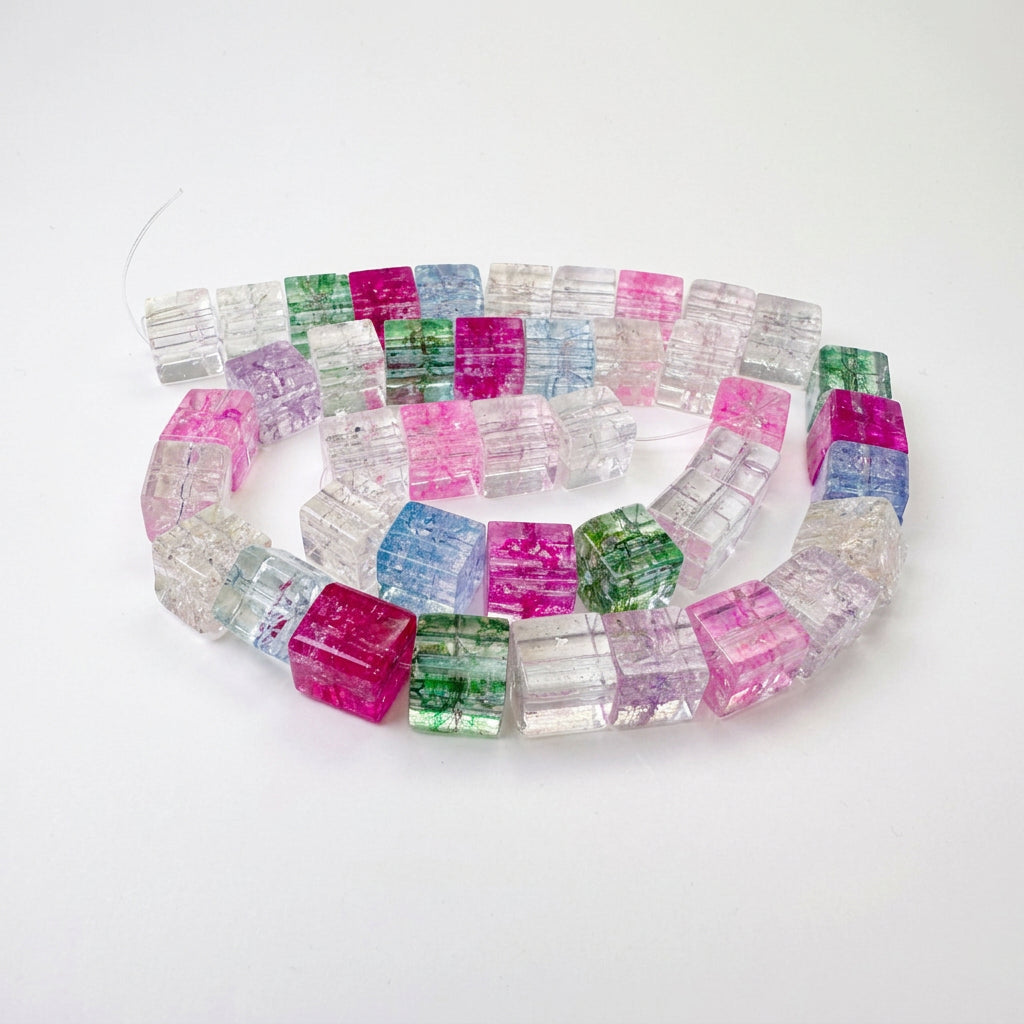 A coiled strand of faceted glass beads in various colors including pink, green, blue, purple, and clear, displayed on a plain light gray surface.