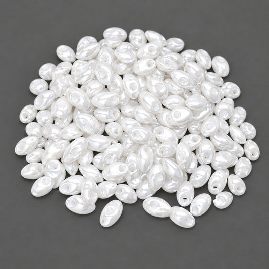 A pile of small, glossy white oval beads with central holes, shown against a dark gray background.